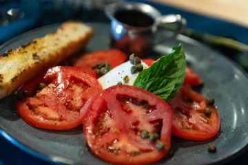 Sliced tomatoes with burrata, basil and capers, grilled bread, and a jug of balsamic
