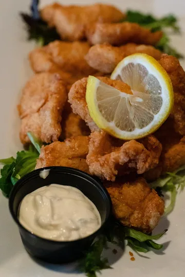 Fried grouper pieces on frisée with a lemon wheel and a ramekin of tartar sauce