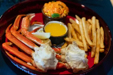 Snow crab legs and claw meat on a red tray with drawn butter, fries and tomato rice